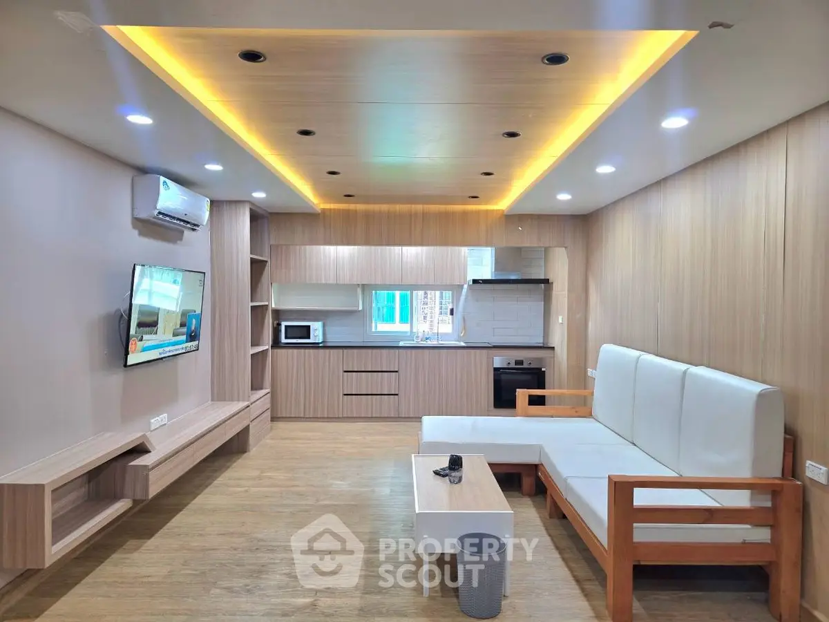 Modern living room with open kitchen, sleek wooden finishes, and cozy seating area.