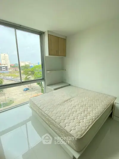 Bright bedroom with large window and city view, featuring a minimalist design and ample natural light.