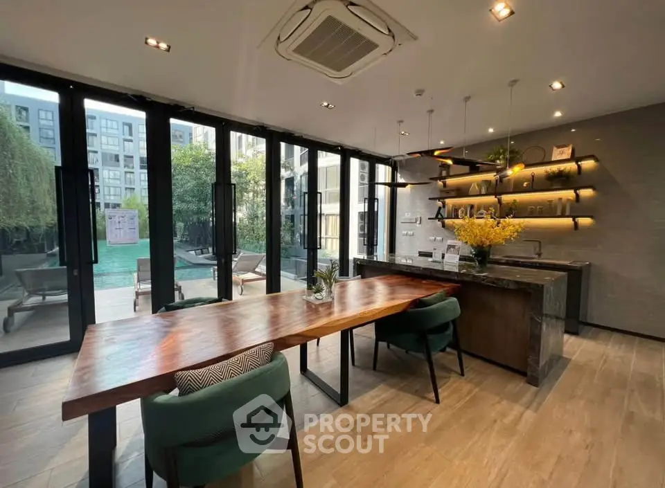 Modern communal area with stylish wooden table and pool view in luxury apartment complex.