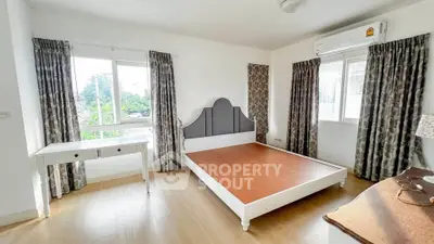 Spacious bedroom with large windows and elegant curtains, featuring a stylish bed frame and wooden flooring.