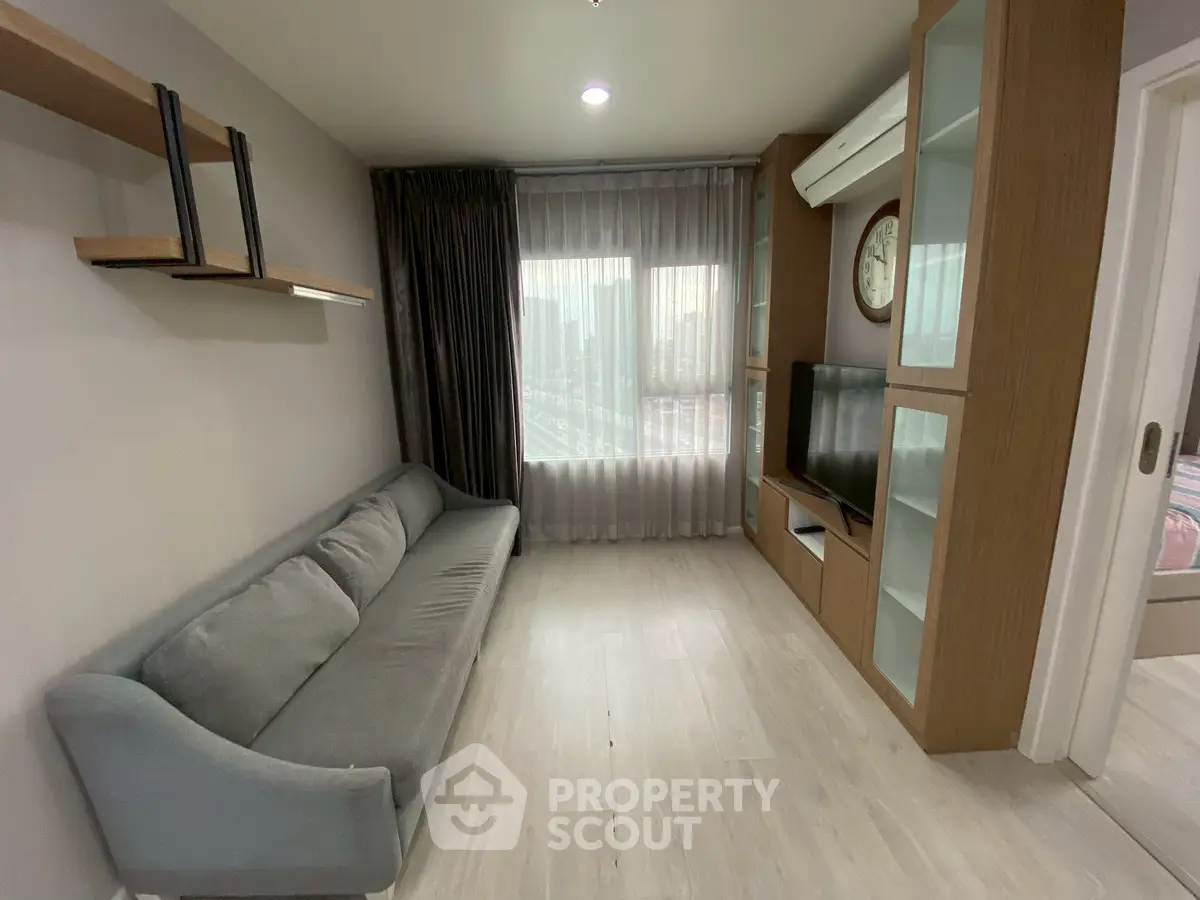 Modern living room with sleek sofa and built-in TV unit, featuring large window with city view.