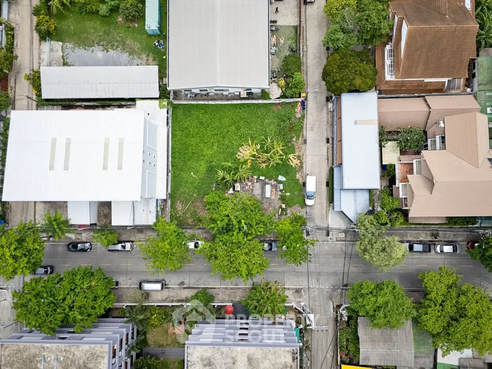 Aerial view of a residential neighborhood with green vacant lot, surrounded by houses and trees.