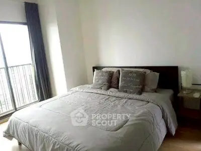 Spacious bedroom with large window and cozy bedding in modern apartment.