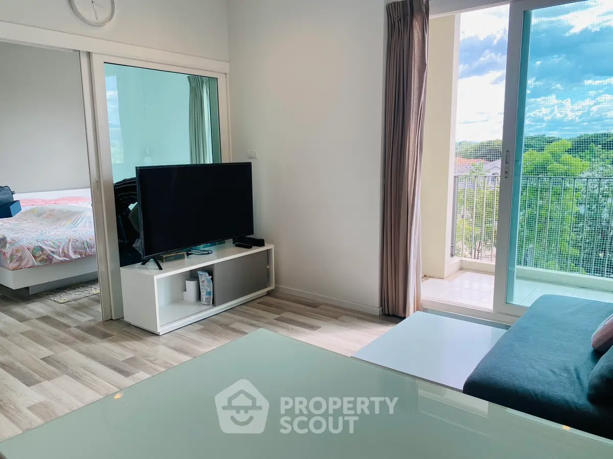 Modern living room with balcony view and adjacent bedroom, featuring sleek furniture and natural light.