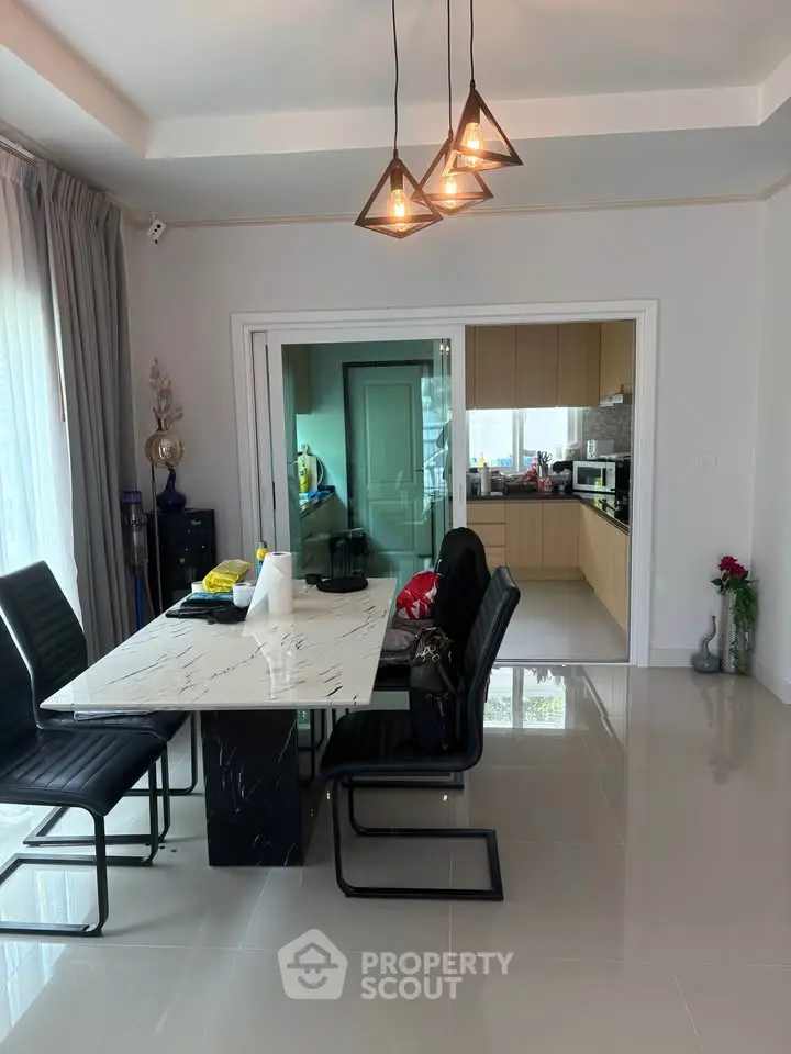 Modern dining area with sleek marble table and stylish lighting adjacent to a contemporary kitchen.
