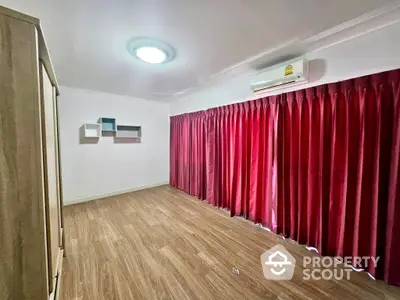 Spacious and well-lit living room with elegant red curtains, modern air conditioning unit, and sleek wooden flooring.