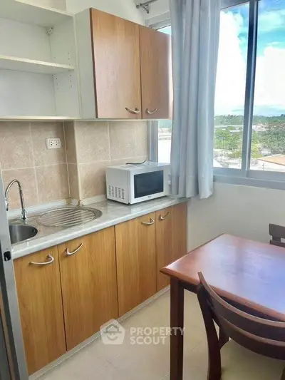 Cozy kitchen with wooden cabinets and microwave, featuring a bright window view.