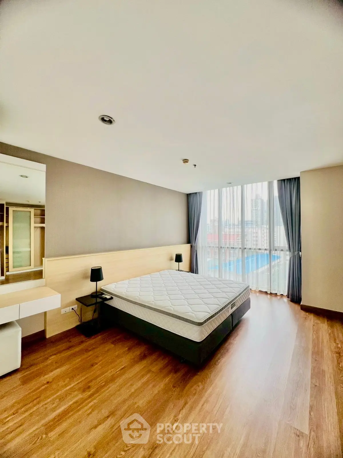 Spacious bedroom with large window and wooden flooring in modern apartment.