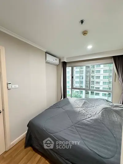 Modern bedroom with large window offering city view in high-rise apartment.