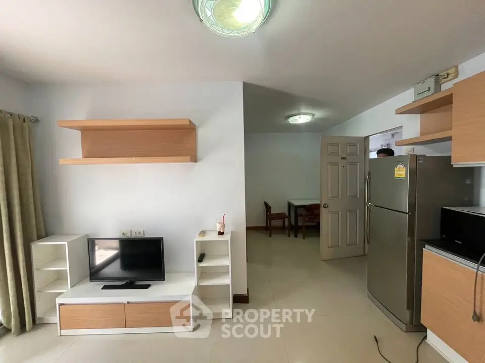 Modern living room with sleek furniture and stainless steel fridge in a cozy apartment.