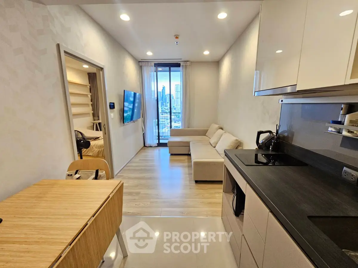 Modern open-plan living room with kitchen, featuring sleek design and city view from balcony.