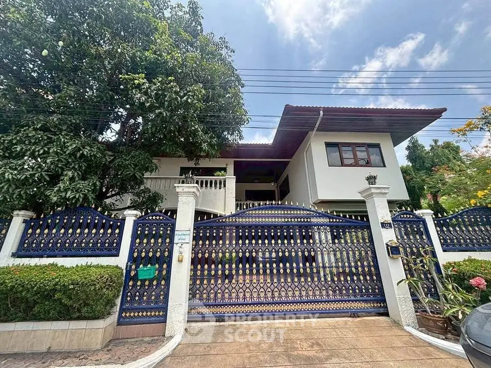 Charming two-story house with ornate gate and lush greenery, perfect for family living.