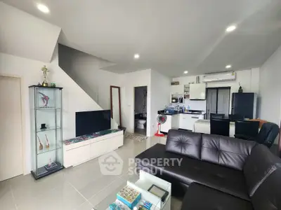 Modern living room with sleek black leather sofa and open kitchen layout, perfect for contemporary living.