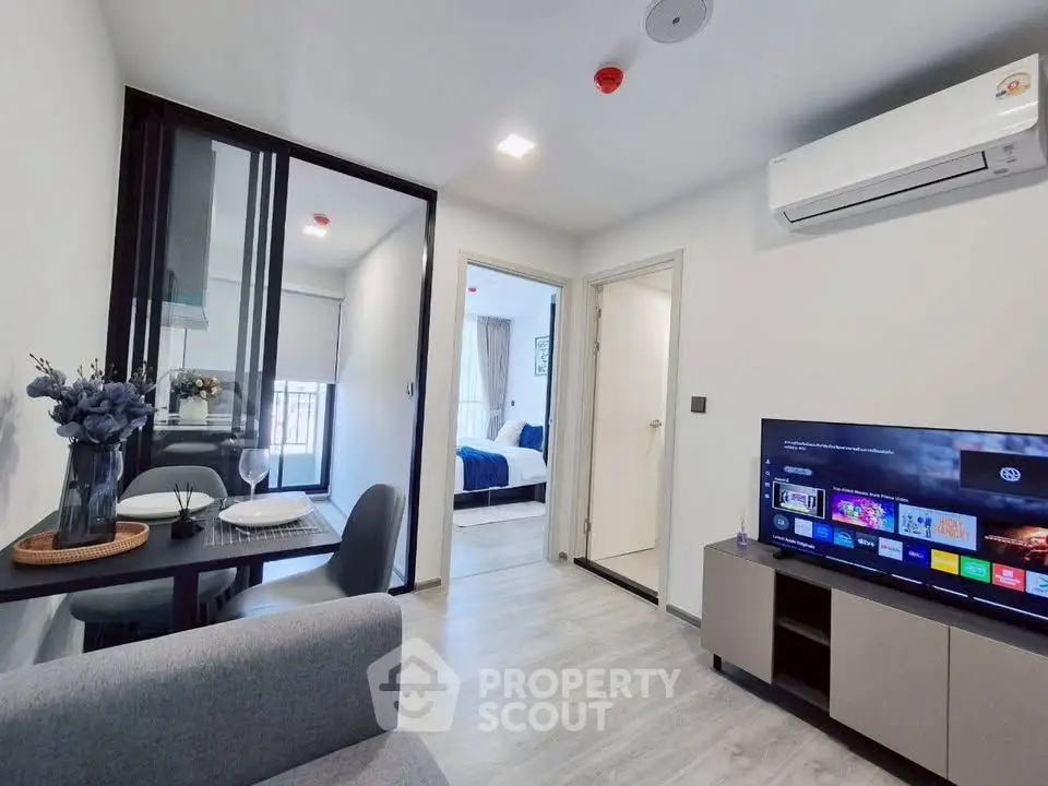 Modern living room with sleek furniture and open view to bedroom, featuring a cozy dining area and wall-mounted TV.