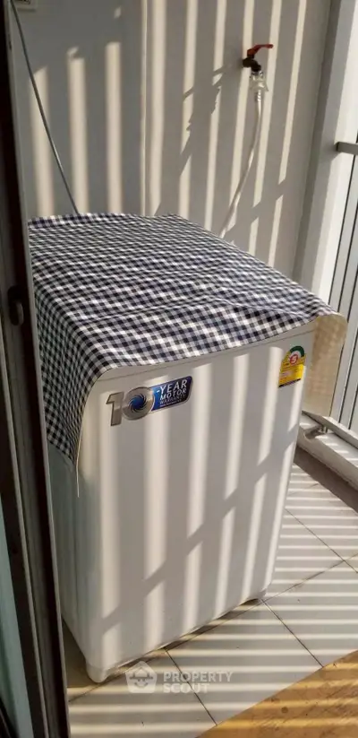 Compact balcony with washing machine and checkered cover, ideal for urban living.