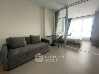 Modern studio apartment with cozy living area and bedroom separated by glass partition.