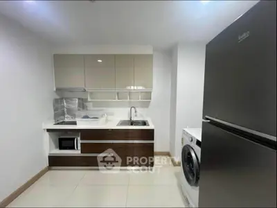 Modern kitchen with sleek cabinetry, stainless steel fridge, and washing machine in a compact layout.