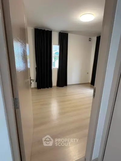 Spacious empty room with wooden flooring and large window, ideal for customization.