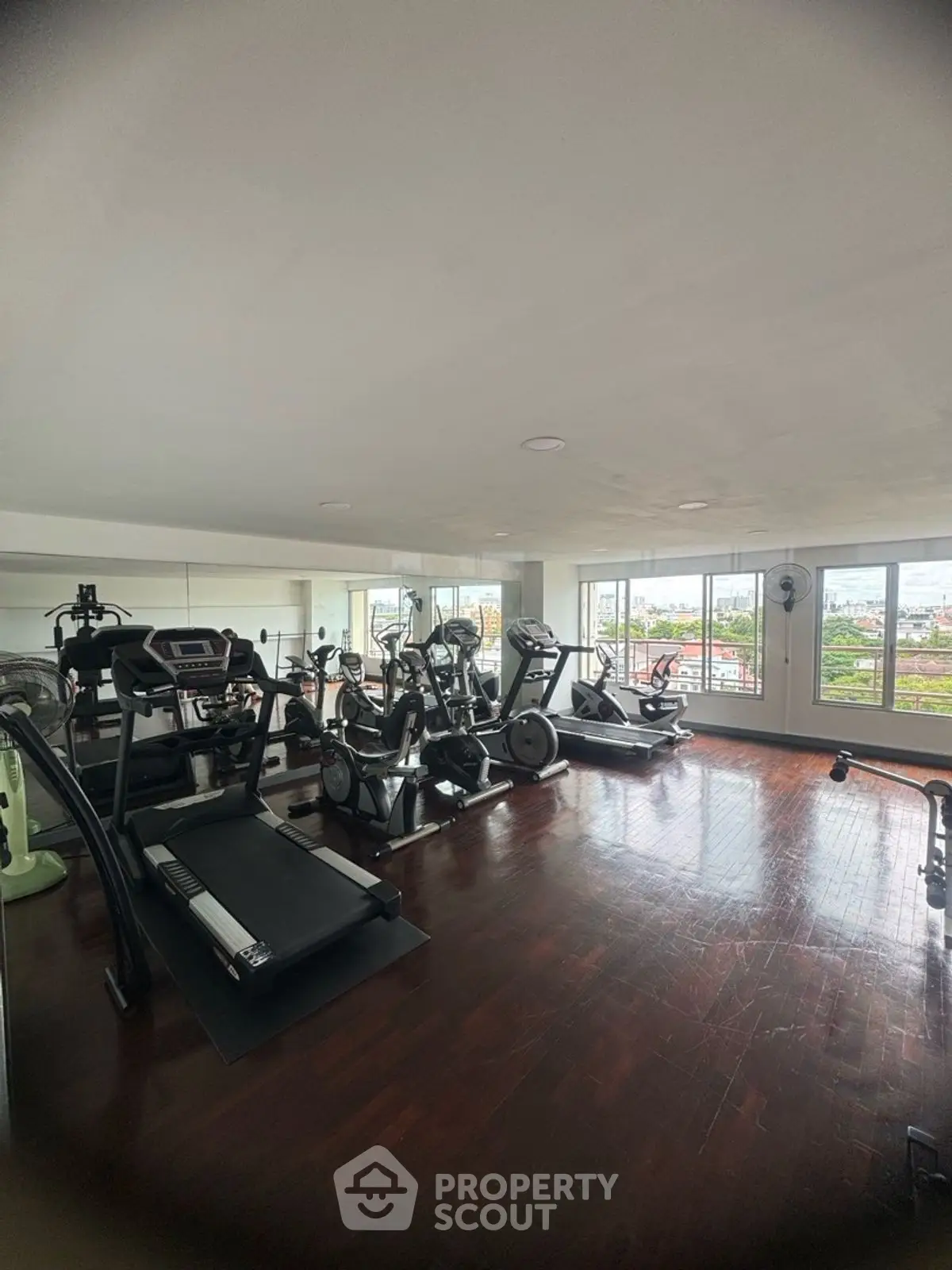 Spacious gym with modern equipment and city view, ideal for fitness enthusiasts.