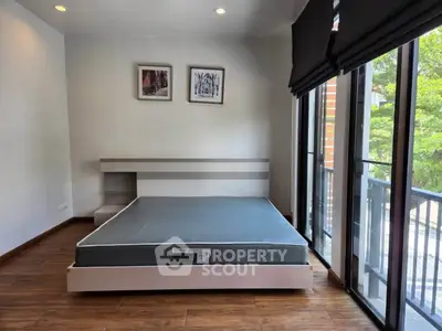Modern bedroom with large windows and balcony view, featuring sleek wooden flooring and minimalist decor.