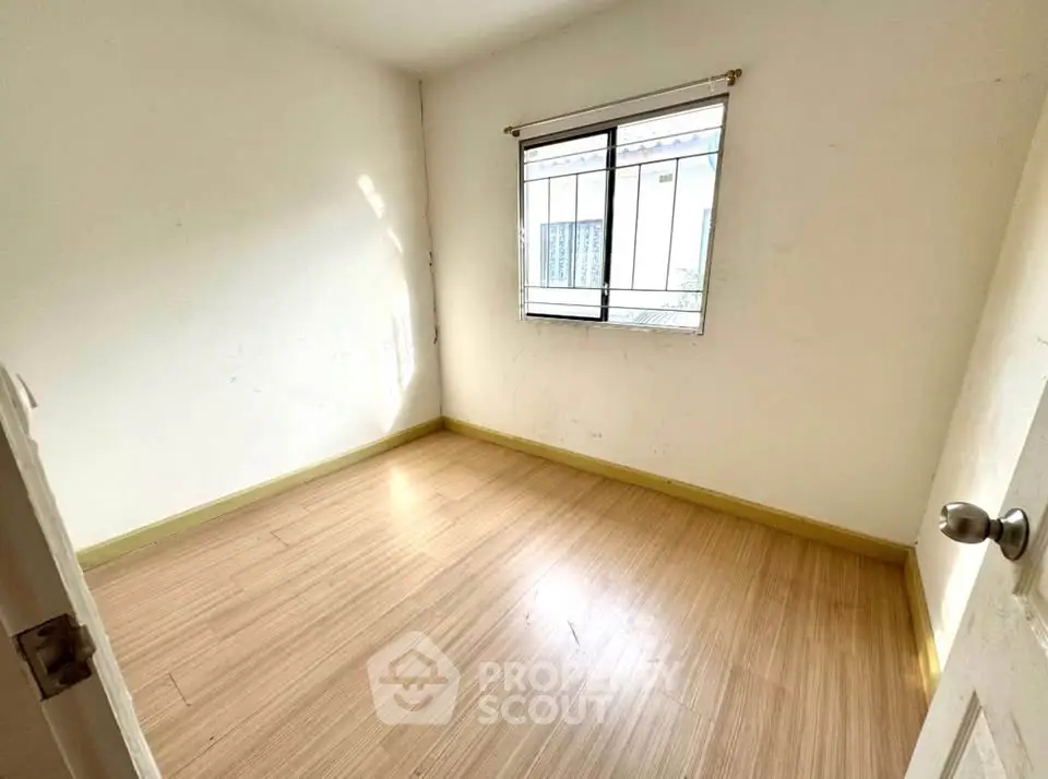 Spacious empty bedroom with wooden flooring and natural light from window.