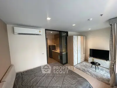 Modern bedroom with sleek design, featuring a cozy bed, air conditioning, and a view into a compact kitchen area.