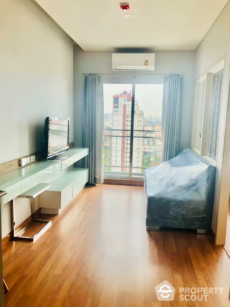 Modern living room with large window and city view, featuring sleek furniture and wooden flooring.