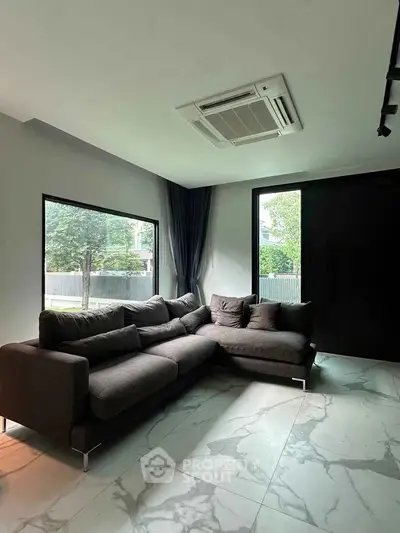 Modern living room with large windows, stylish L-shaped sofa, and elegant marble flooring.