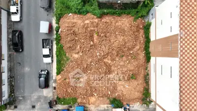 Aerial view of an empty urban plot ready for development, surrounded by buildings and street access.