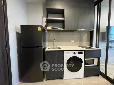 Modern compact kitchen with sleek black cabinets, washing machine, and fridge in a stylish apartment.