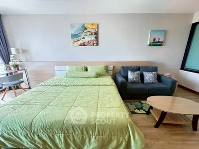 Modern bedroom with green bedding, cozy sofa, and stylish decor in a bright apartment.