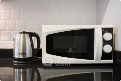 Modern kitchen with microwave and electric kettle on sleek countertop.