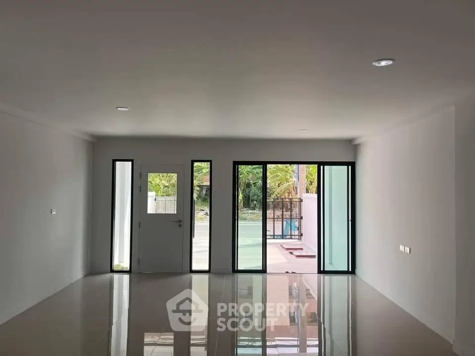 Spacious modern living room with large windows and glossy tiled floor, offering abundant natural light.