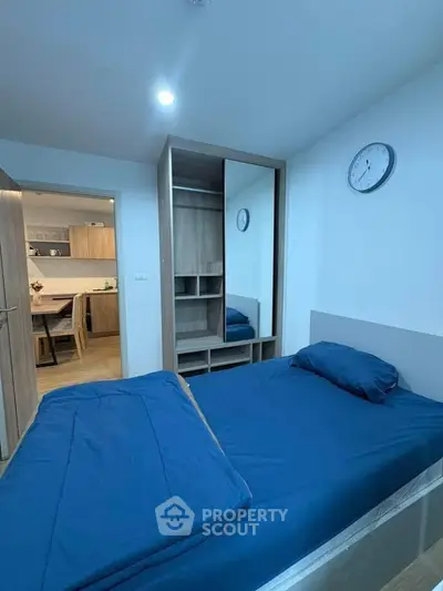 Modern bedroom with blue bedding and open closet, adjacent to a stylish kitchen area.