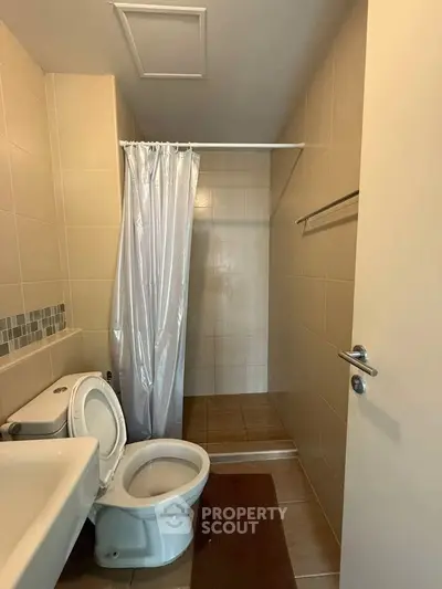 Compact bathroom with shower curtain and tiled walls, featuring a toilet and sink.