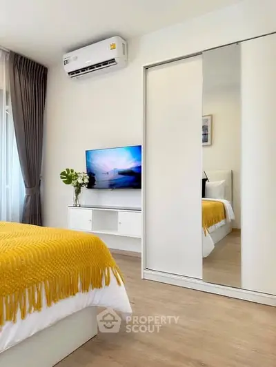 Modern bedroom with stylish decor, mirrored closet, and wall-mounted TV