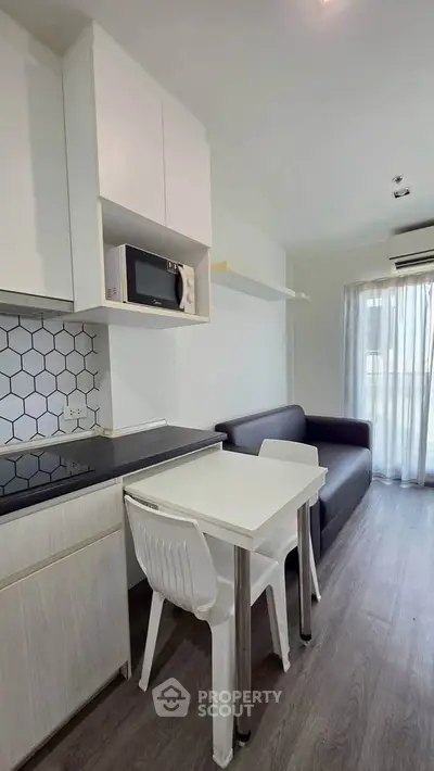 Modern compact living room with kitchenette, featuring sleek design and natural light.