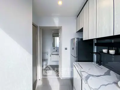 Modern kitchen with sleek cabinetry and marble countertops leading to a compact bathroom.