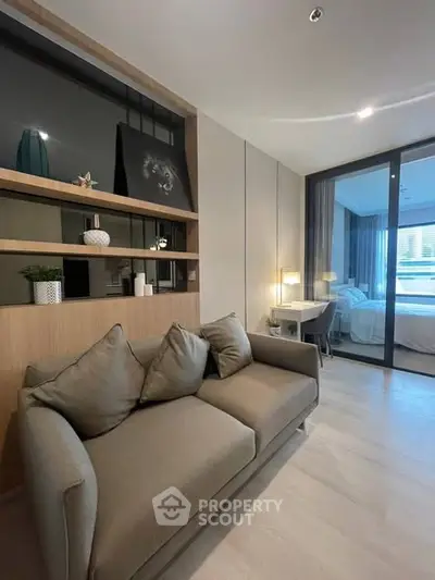 Modern living room with cozy sofa and stylish decor, featuring a view into a chic bedroom through glass doors.