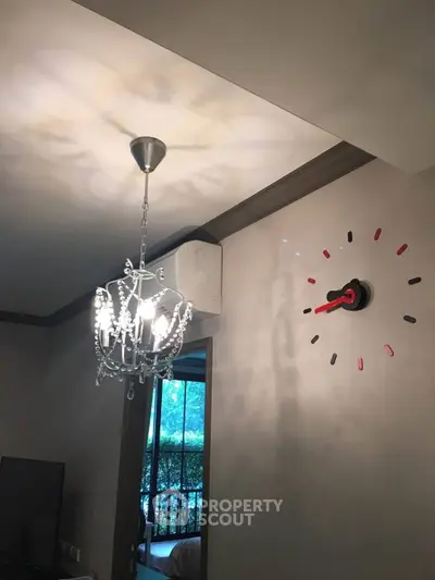Elegant living room with chandelier and unique wall clock design, offering a glimpse of lush greenery outside.