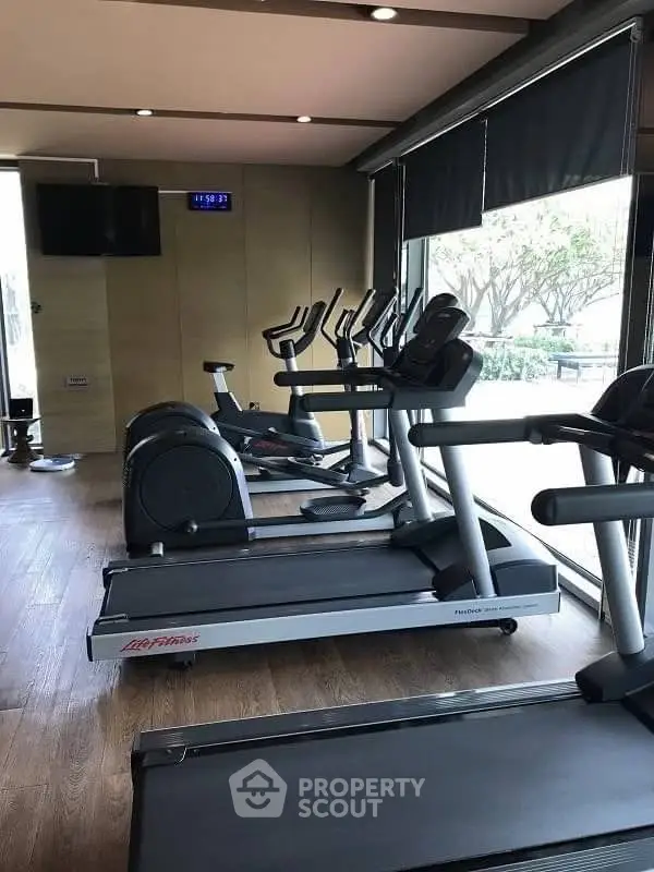 Modern gym with treadmills and exercise bikes in a well-lit space with large windows.