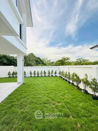 Spacious backyard with lush green lawn and modern white exterior, perfect for outdoor activities.