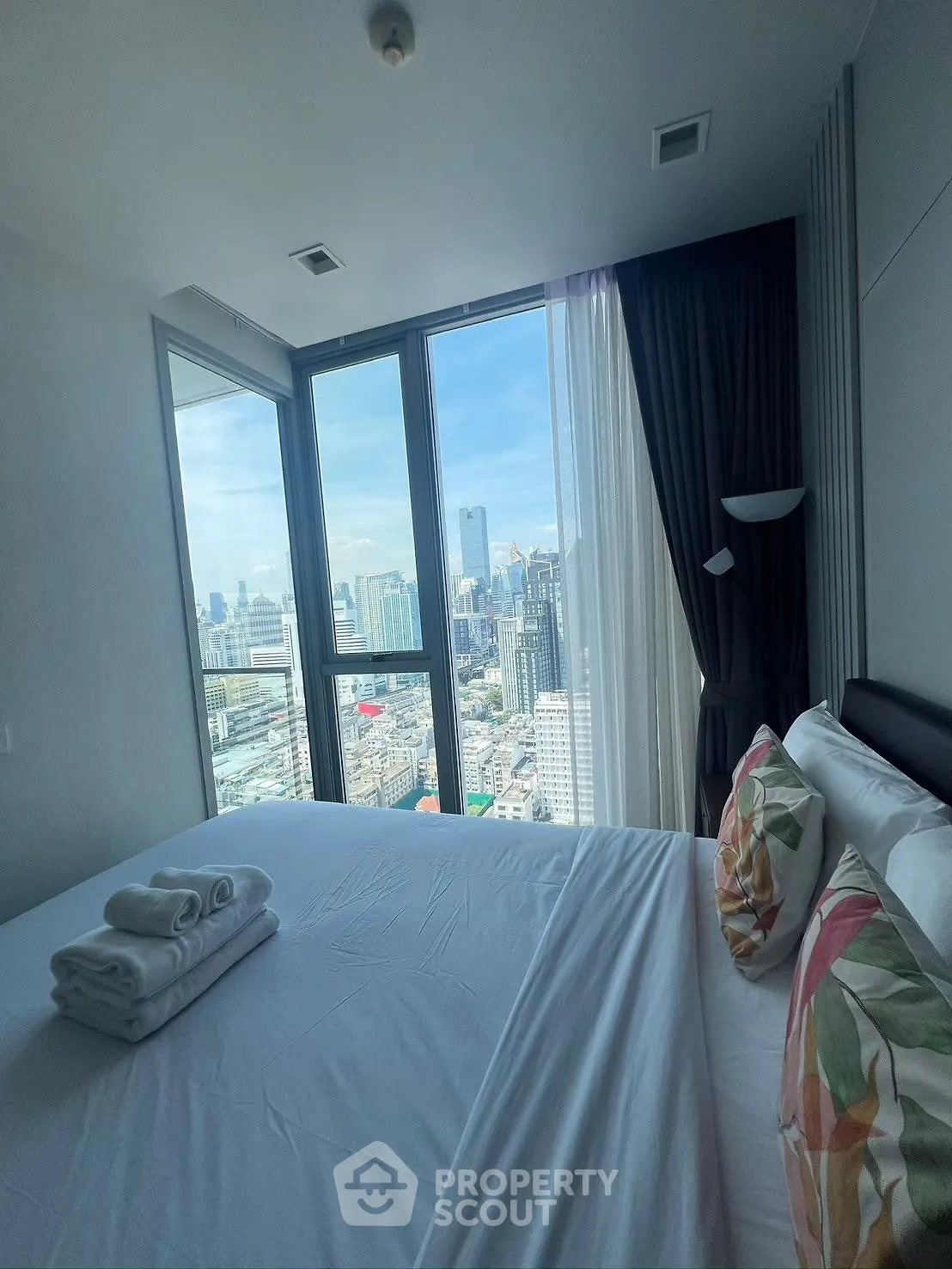Luxurious bedroom with panoramic city view from floor-to-ceiling windows.