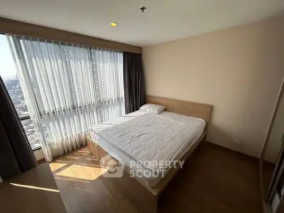 Bright and cozy bedroom with large window and wooden flooring in modern apartment.