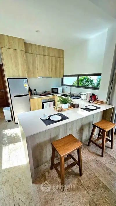 Modern kitchen with open layout, featuring wooden cabinets, breakfast bar, and natural light.