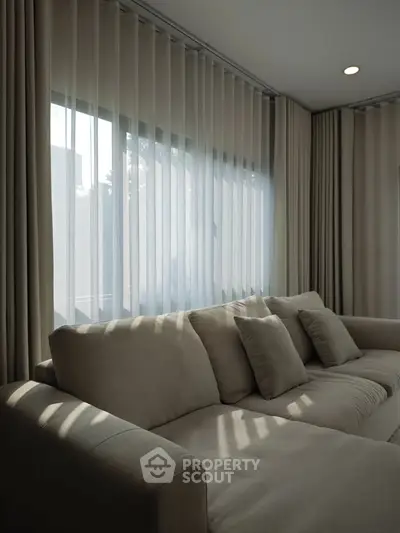Elegant living room with plush beige sofa and floor-to-ceiling windows with sheer curtains.