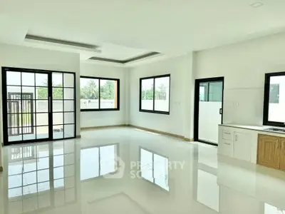 Spacious modern living room with large windows and sleek kitchen area, perfect for natural light lovers.