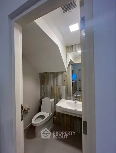 Modern bathroom with sleek design and stylish wood paneling under staircase.