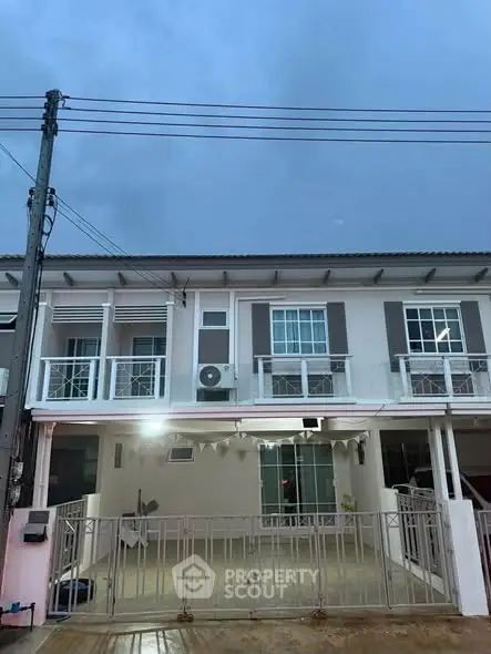Charming two-story townhouse with gated front yard and modern facade under a cloudy sky.