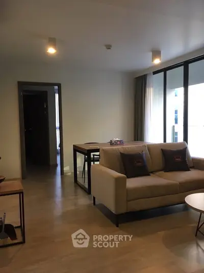 Modern living room with cozy sofa and dining area, featuring large windows for natural light.